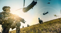 Italian soldiers in camouflage uniforms position themselves in a grassy field as military aircraft operate overhead during a training exercise.