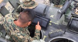 Service member in camouflage uniform uses a rugged tablet displaying GeoSuite tactical mapping software inside an armored vehicle.