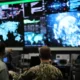 Military personnel viewing large digital screens displaying global data and operational information inside a command center.