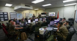 Military command center with personnel monitoring multiple data screens during training exercise
