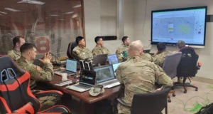 Soldiers in a command center monitor digital maps and data feeds during a multi-domain military training exercise.
