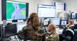 German military command center with personnel analyzing real-time battlefield data across multiple digital screens