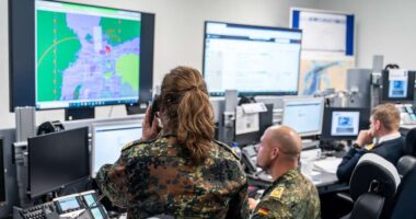 German military command center with personnel analyzing real-time battlefield data across multiple digital screens