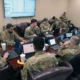 Anthropic vs Pentagon | US servicemembers in uniform use laptops during a cybersecurity assessment in a government facility.