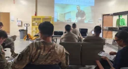 Military personnel attending a medical training session with a projected instructional screen