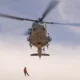 Military helicopter hoisting a rescue personnel during a search and rescue operation in a dusty environment