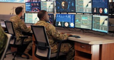 US Air Force personnel in uniform analyzing multiple digital dashboards and data feeds inside a command and control center. USAF data strategy