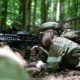 US Army National Guard soldier takes cover during infantry training exercise in wooded terrain.