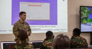 U.S. Army cyber specialist briefs Tanzania People’s Defence Force personnel during a cyber defense training session, with network security and cyber operations materials displayed on a projection screen in Dar es Salaam, Tanzania.